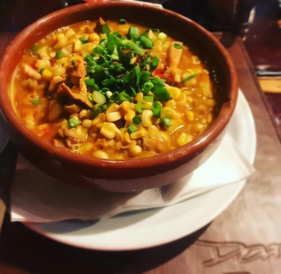 Cazuela de barro con guiso de choclo y verdeo sobre plato blanco
