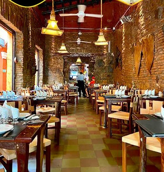 Salón largo con ladrillo visto, piso damero y mesas de madera puestas